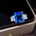 Macro detail of emerald-cut blue gemstone ring with rectangular side stones on black velvet - US 6 / Blue