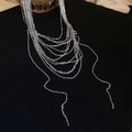 Macro detail of minimalist silver layered necklace chains draped over a dark background - Silver