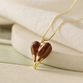 Detailed close-up of brown heart pendant with golden liquid drip on fine link chain - Coffee