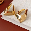 Close-up of gold-plated irregular geometric earrings on a textured linen notebook - Gold