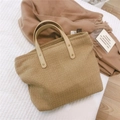 Detail of khaki woven tote bag with smooth brown handles and golden rivets on white surface - Light Camel