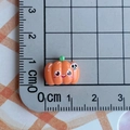 Detailed view of mini Halloween pumpkin resin charm showing 1.5 cm size on a ruler - Big-eyed Smiling Pumpkin