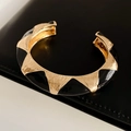 Dettaglio del bracciale rigido vintage in metallo con smalto nero su pelle nera - Stile Aperto Largo / Contrasto Oro e Nero