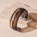 Primer plano de brazalete de resina ámbar sobre piedra travertino beige con luz cálida - Negro