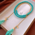 Dettaglio di perle turchesi con nappe dorate vintage e ciondoli a foglia sulla catena - Verde