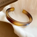 Gros plan d'un bracelet ouvert en résine ambrée translucide sur une assiette en céramique - Style Carré Café (2#)