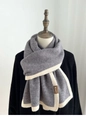 Detail of grey and beige knit scarf featuring a brown textured label and striped pattern - Gray