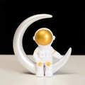 Astronautenbeeldje zittend op een witte halve maan met gouden helmaccenten - Gouden Maan