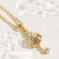 Macro detail of a golden key pendant with an opal-like stone and Saturn ring design - Skeleton Key Necklace