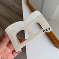 Dettaglio di un fermaglio per capelli a forma di B color crema perlato in acetato lucido - Bianco Sirena B Molletta