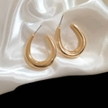 Nahaufnahme goldener U-förmiger Creolen auf weißem Seidenstoff mit eleganter Metallstruktur - Gold