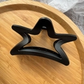 Detailed view of large black matte star-shaped hair claw clip on a rustic wooden tray - Black