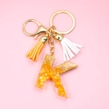 Macro shot of resin letter K keychain with orange stones, gold ring and fringe tassel - Letter K