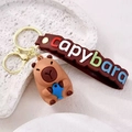 Porte-clés Capybara marron avec petit poisson bleu et dragonne en silicone - Tenant un Poisson