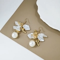 Detalle de pendientes de delfín dorados con pétalos blancos y perlas sobre fondo de cuero - Ballena/Delfín