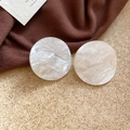 Macro detail of round white acrylic earrings with marble texture on dark fabric - White