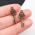 Coppia di ciondoli a chiave in bronzo antico sulle dita per mostrare le dimensioni - Chiave in Bronzo Antico 22x9mm