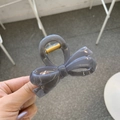Detail of grey glossy acrylic bow hair claw clip with golden metal spring shown by hand - Approx. 8cm / Light Silver Grey