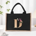 Black canvas tote bag with golden letter D and floral print on white desktop - Bronze Floral Letter D