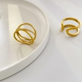 Detailopname van gouden golvende ringen en minimalistische gedraaide band op een wit dienblad - US 6 / Drielaags Kruislings