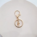 Detailed close-up of gold metal lobster clasp keychain parts on a ceramic tray - Lobster Clasp + Flat Ring + 4-Link Chain / Gold 4-Link Style