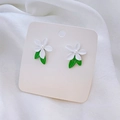 Detalle de pendientes de flores blancas con hojas verdes y perlas sobre seda - Pendiente De Flor De Perla