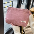 Close-up of pink corduroy makeup bag with MAY RABBIT label held in a cafe setting - Flesh Pink