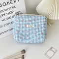 Detail of blue quilted cosmetic bag with pink bow patterns and woven brand label - Blue Gingham Bow
