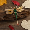 Spilla a libellula con gemma verde e ali gialle su sfondo in legno scuro elegante - Libellula in Giada Artificiale Ali Arancioni / Arancione