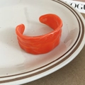 Macro shot of an orange acrylic bangle with irregular wave texture on a ceramic plate - Orange