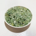 Polished natural green peridot crystal stone chips in a white ceramic bowl on a wooden desk - Prehnite