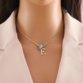 Detail of gold letter E pendant necklace with blue bead on a model's neck - Letter E (N1339)