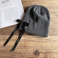 Dettaglio berretto grigio scuro in maglia con fiocco di raso nero su sfondo in legno - M / Grigio Melange