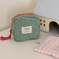 Close-up of green and white plaid quilted pouch with orange metal zipper and logo tag - Green