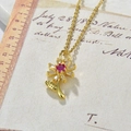 Close-up of golden sunflower pendant with pink and white zircon beside a vintage ruler - Sunflower Necklace / Deep Pink