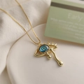 Detailed shot of golden Evil Eye pendant with blue stone and teardrop on white plate - Style 1 / Gold