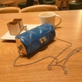 Blue quilted cylindrical jelly bag with gold chain strap on a wooden table - Transparent Blue