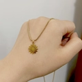 Detail of 18K gold daisy pendant on sleek snake chain held in hand for scale - Daisy
