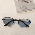 Close-up of minimalist black metal oval frames with light blue tinted lenses on beige background - Black Frame Light Grey