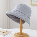 Light gray seersucker bucket hat with metal emblem on a wooden display stand - 80846 Blue