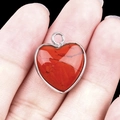 Red heart stone pendant with natural black veins in a silver frame held by hand - Red Jasper Silver Edging