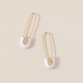 Detailed macro view of gold safety pin earrings with white enamel finish on fabric - White