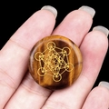 Hand holding a round Tiger Eye stone disc with a golden Metatron's Cube sacred geometry - Tiger's Eye