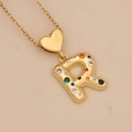 Detailed view of golden letter R heart pendant with colorful zircon stones on beige fabric - Letter R / Gold