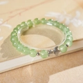 Detailed close-up of light green jade beads with a silver fish charm on a vintage book - Green