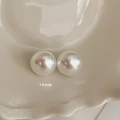 Dettaglio di orecchini di perle bianche da 16mm esposti in una ciotola di ceramica minimalista - Stile Bottone 16mm (MY35435)