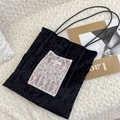 Close-up of black textured canvas bag featuring delicate floral lace embroidery and leather straps - Pink Lace + Black Velvet