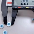 Blue 10mm round shell evil eye bead being measured by a digital caliper for DIY jewelry - 10mm