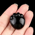 Pendentif en agate noire polie en forme de patte de chat tenu à la main pour taille - Obsidienne