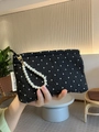 Close-up of black polka dot quilted clutch with elegant pearl handle and brand label - Black Polka Dot